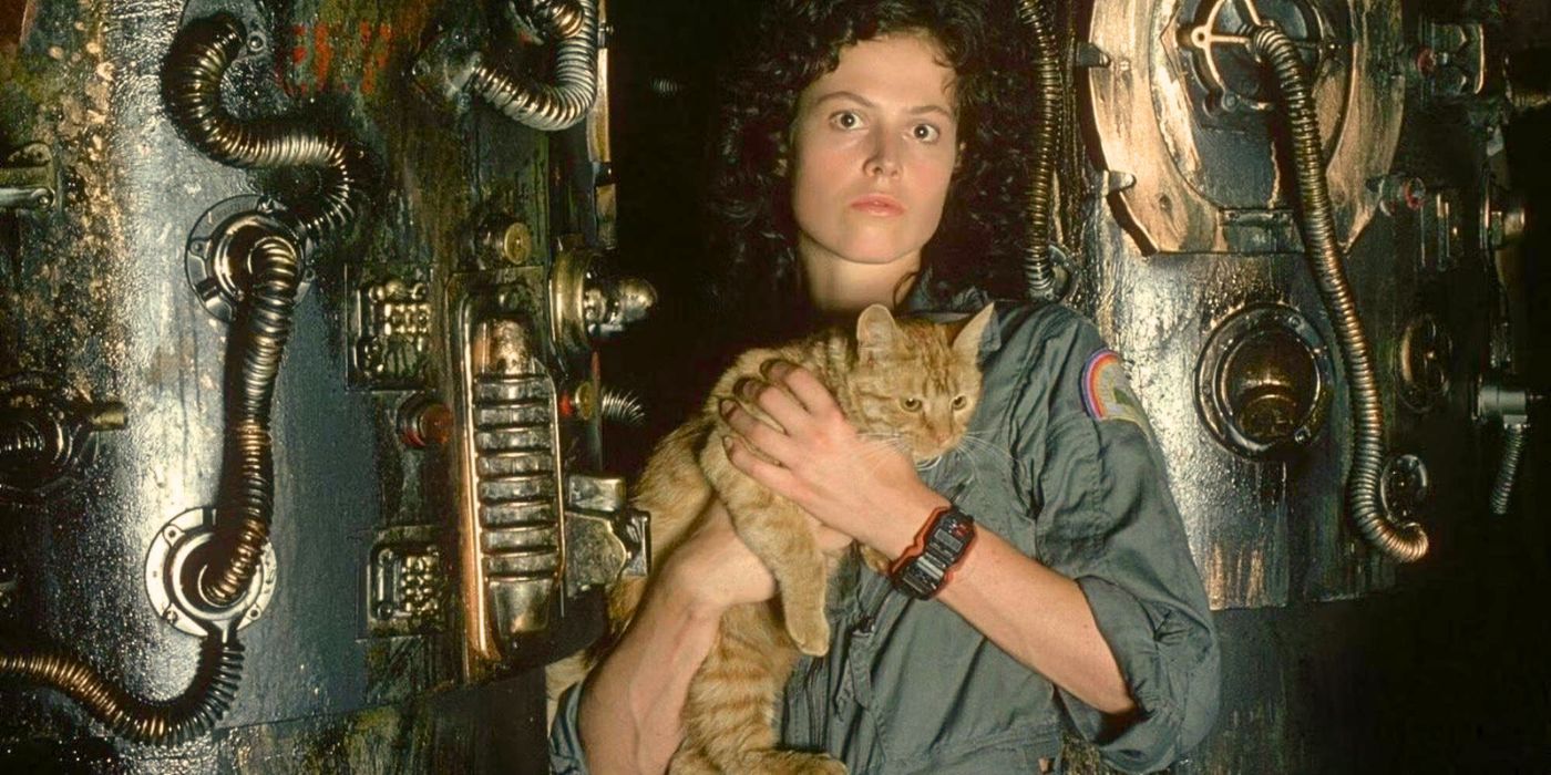 Sigourney Weaver holds an orange tabby space cat while standing in front of spaceship equipment from the movie Alien