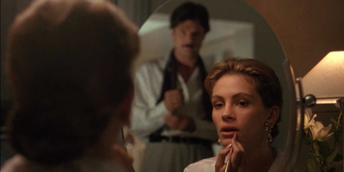 Laura applying lipliner while Patrick Bergin appears behind her