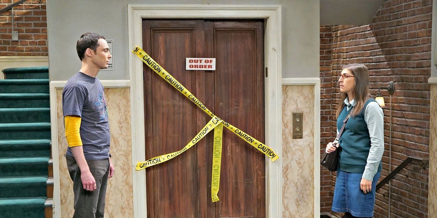 Sheldon and Amy standing on either side of the broken elevator on The Big Bang Theory looking at one another.