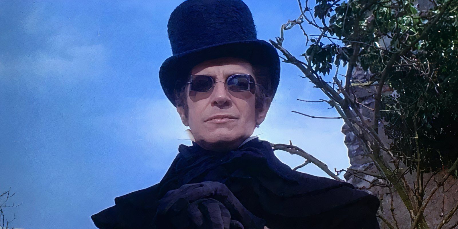 Verden Fell wearing a top hat and black shades looking ahead in The Tomb of Ligeia