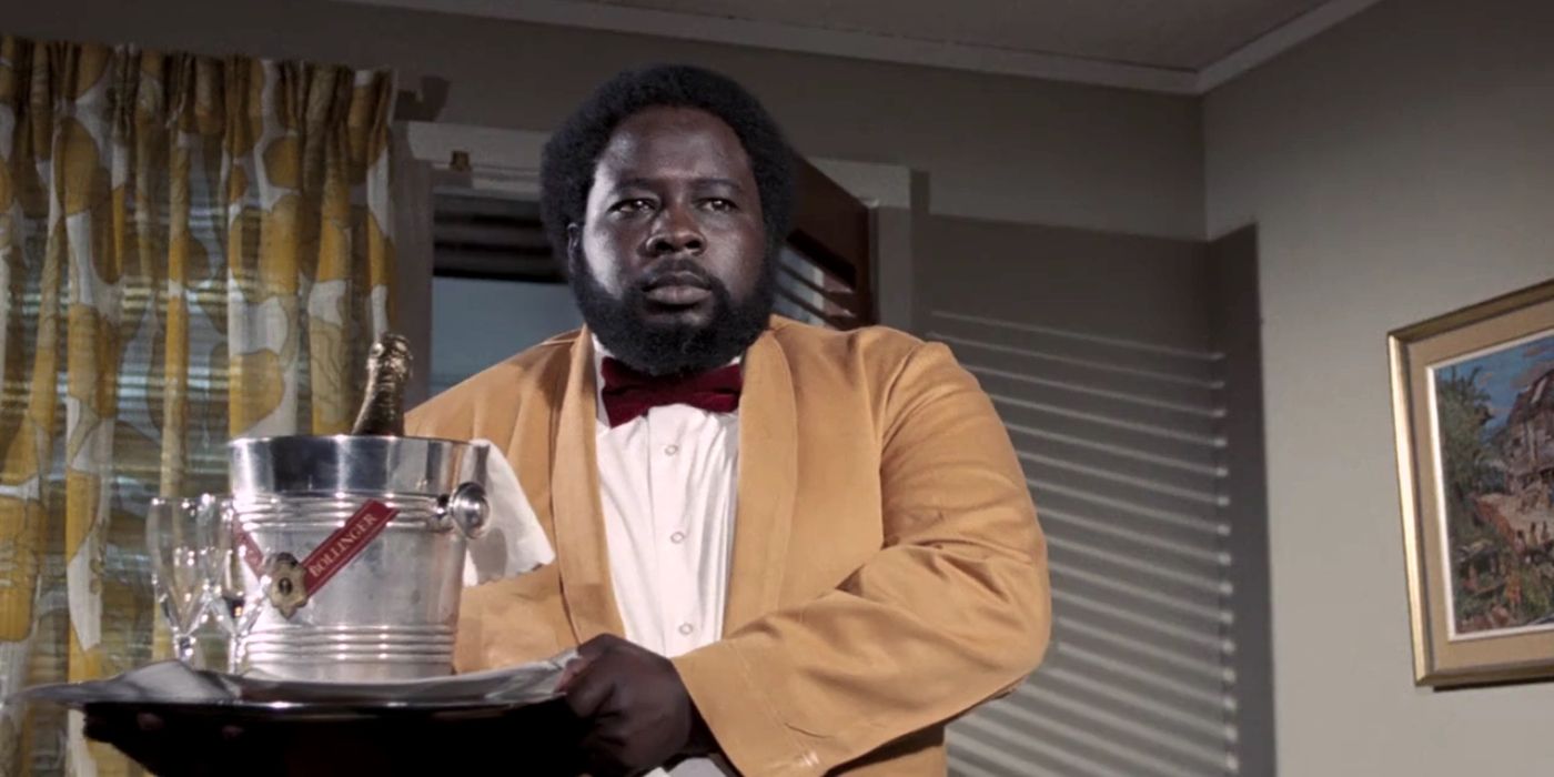 Whisper (Earl Jolly Brown) stands in a yellow tuxedo posing as hotel staff as he delivers a bottle of champagne in &lsquo;Live and Let Die&rsquo; (1973).