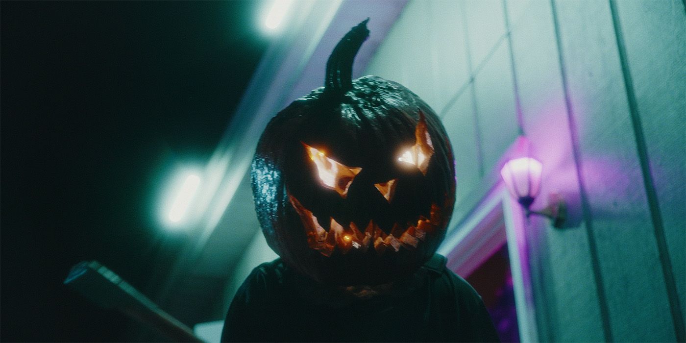 Una persona que lleva una calabaza en la cabeza rodeada de luces de neón de Haunt Season.