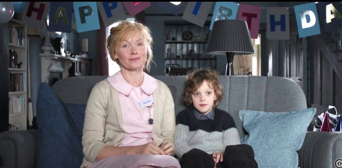 Essie Davis and Noah Wiseman as Amelia and Sam sitting together on a couch in front of a birthday banner in &ldquo;The Babadook&rdquo;