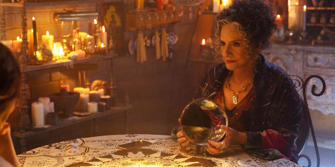 Patti LuPone at a table holding a crystal ball in a room surrounded by candles