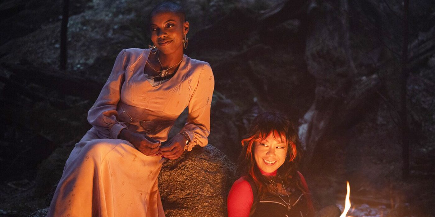 Sasheer Zamata and Ali Ahn smiling in front of a campfire in the woods