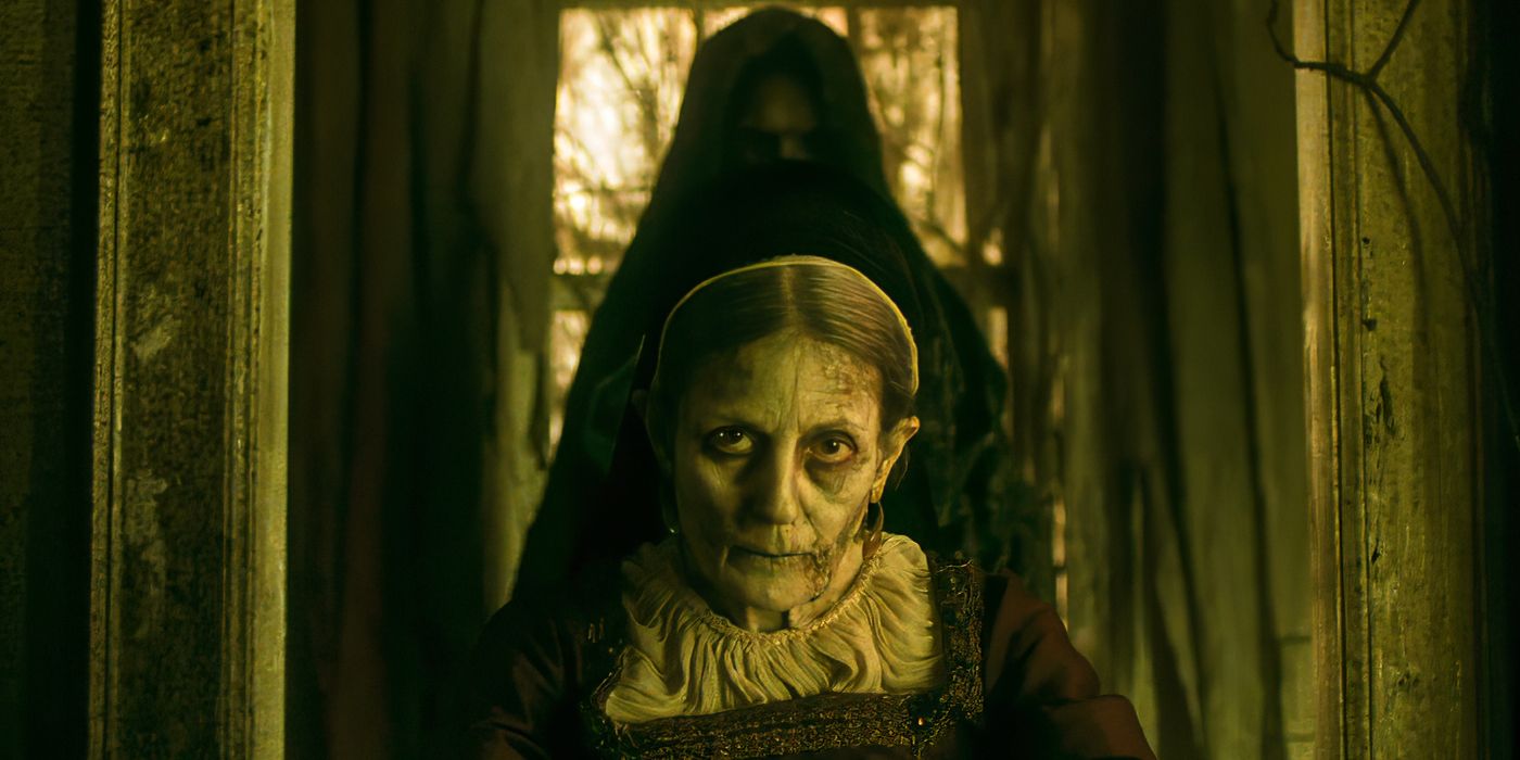 The spirit of Maestra (Laura Boccaletti) stares at the camera with a dark figure behind her in Agatha All Along.