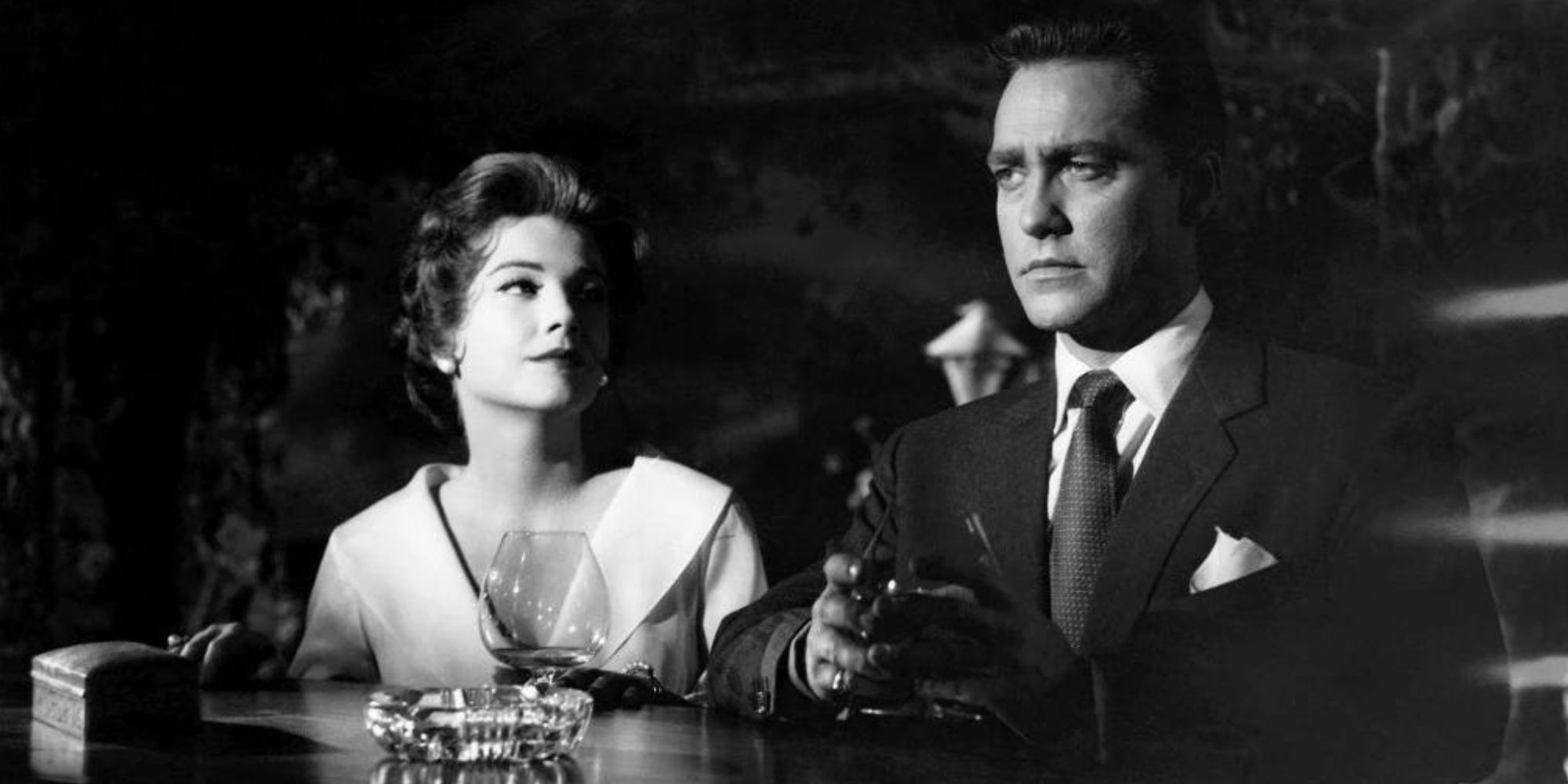 Anne Baxter sitting at a bar next to Richard Todd in Chase a Crooked Shadow (1958)