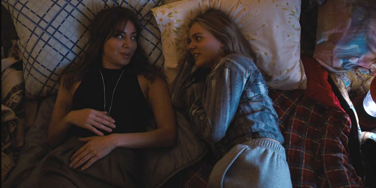 Aubrey Plaza as an older Elliott and Maisy Stella as a younger Elliott lay in bed together in My Old Ass