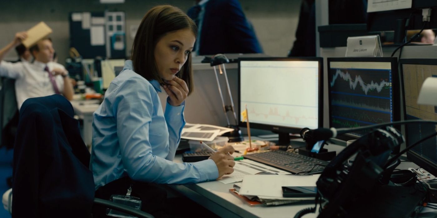 Yana Reekum (Paula Beer) is looking at a chart on her computer. She holds a pen in her right hand and her left hand rests on her chin. 