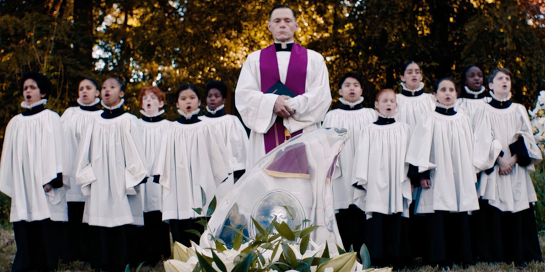 Burn Gorman as priest Father Damien conducting a funeral service in front of a choir in Beetlejuice Beetlejuice