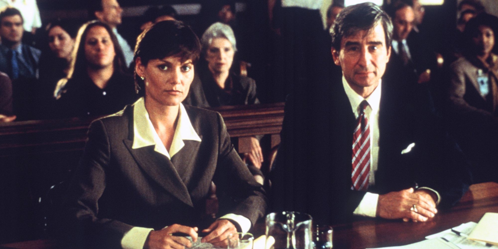 Carey Lowell e Sam Waterston sentados juntos à mesa da promotoria em uma sala de tribunal em Law & Order