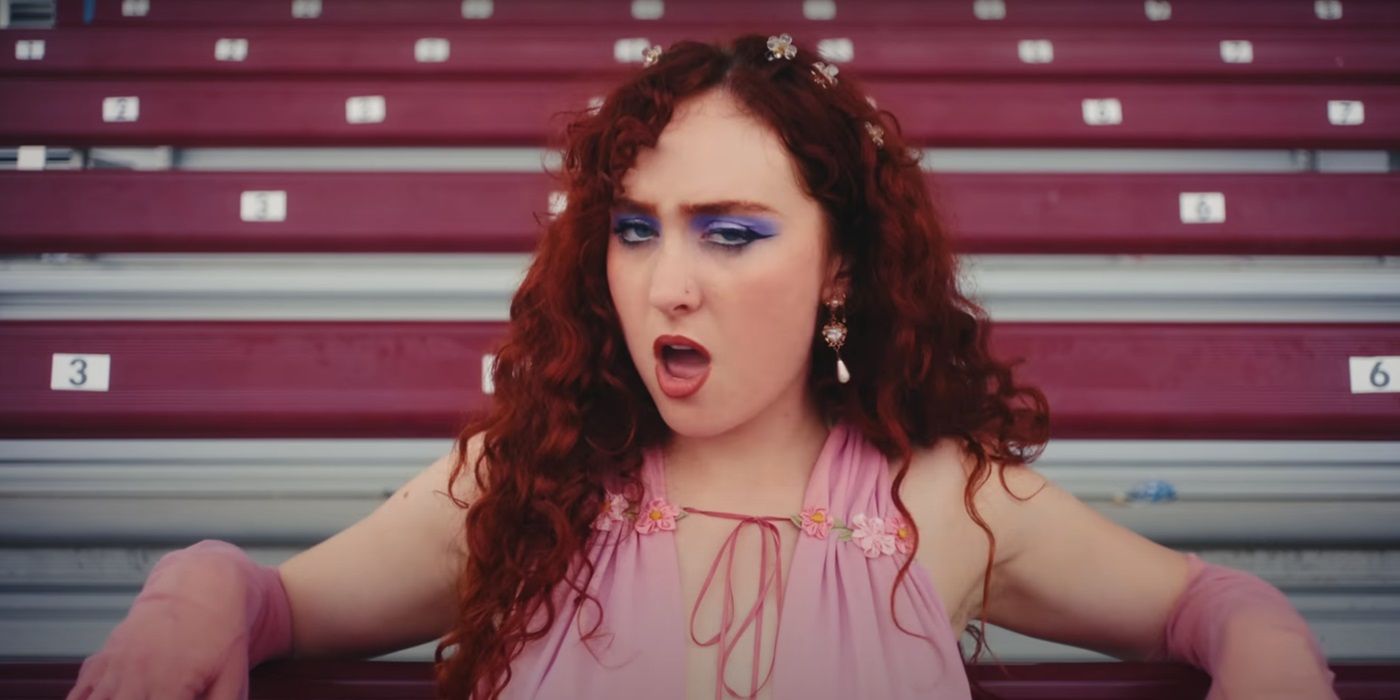 Chapell Roan, in her music video for "HOT TO GO", leans on bleachers and sings