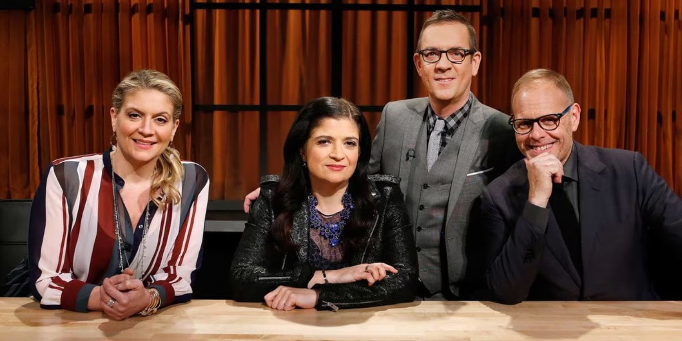 The hosts of Chopped sit at a wooden table and pose for a promotional photo.