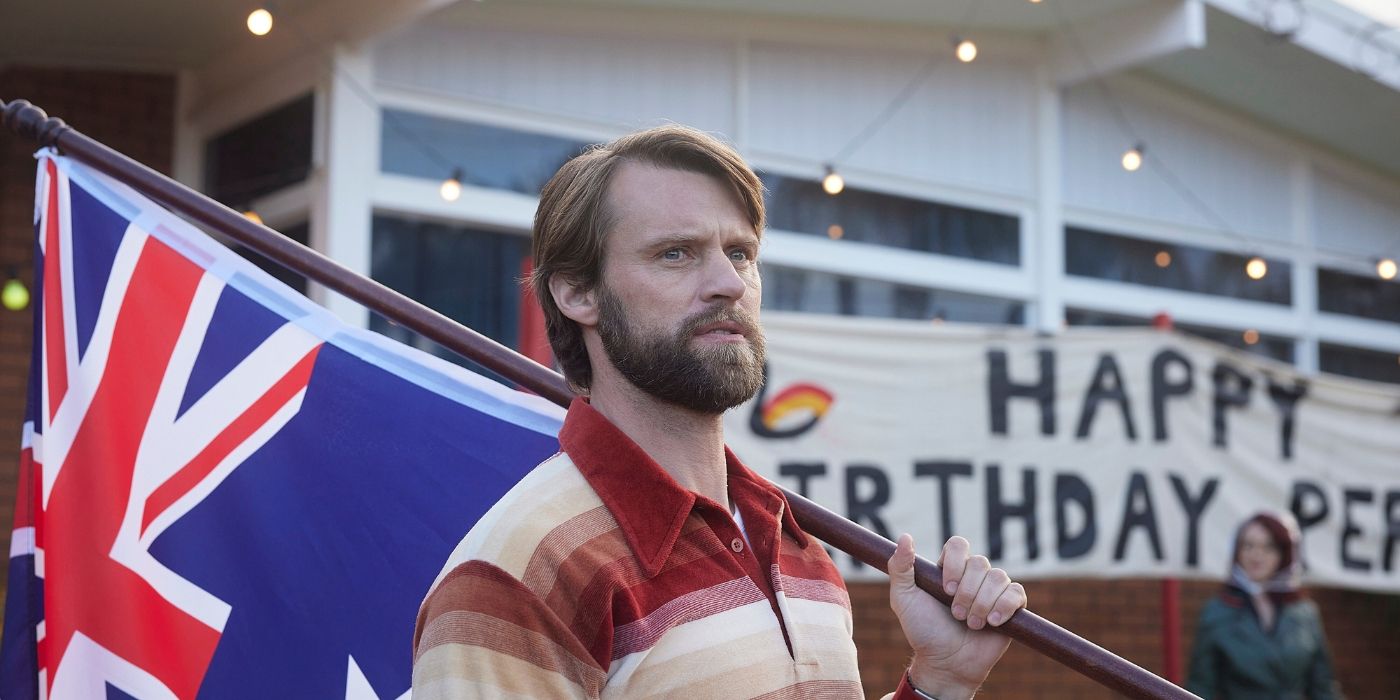 Jesse Spencer holding a flag at an outdoor celebration for the town in Last Days of Space Age