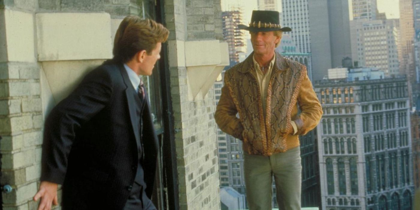 Crocodile Dundee (Paul Hogan) stands casually on a ledge with a man in a suit in 'Crocodile Dundee II' (1988).