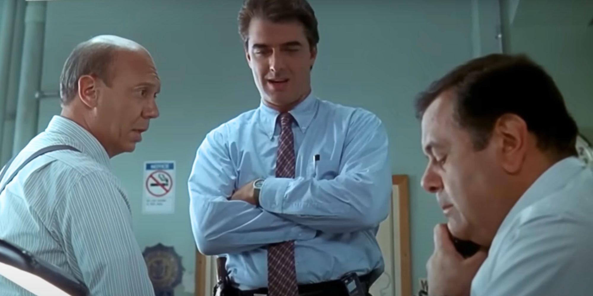 Dan Florek and Chris Noth stand around Paul Sorvino as he sits at his desk talking on the phone in the Law & Order episode 