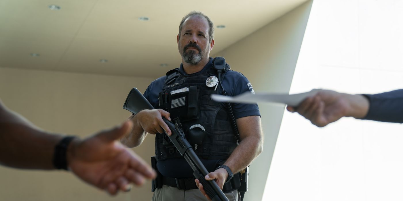 David Denman, quien interpreta al ayudante del sheriff Evan Marston en Rebel Ridge, sostiene una escopeta mientras le entregan papeles frente a él.