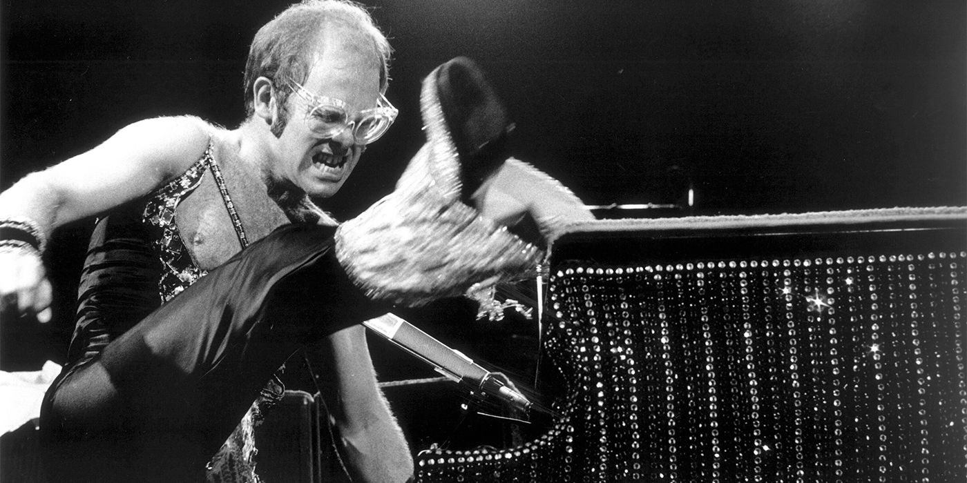 Black and white photo of young Elton John vigorously playing piano with his foot