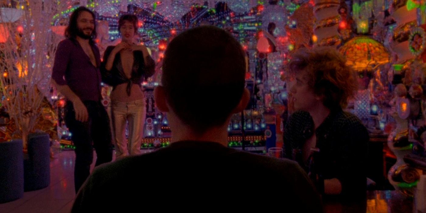 Two people are talking with others in the background with lots of party looking lights in Enter the Void.