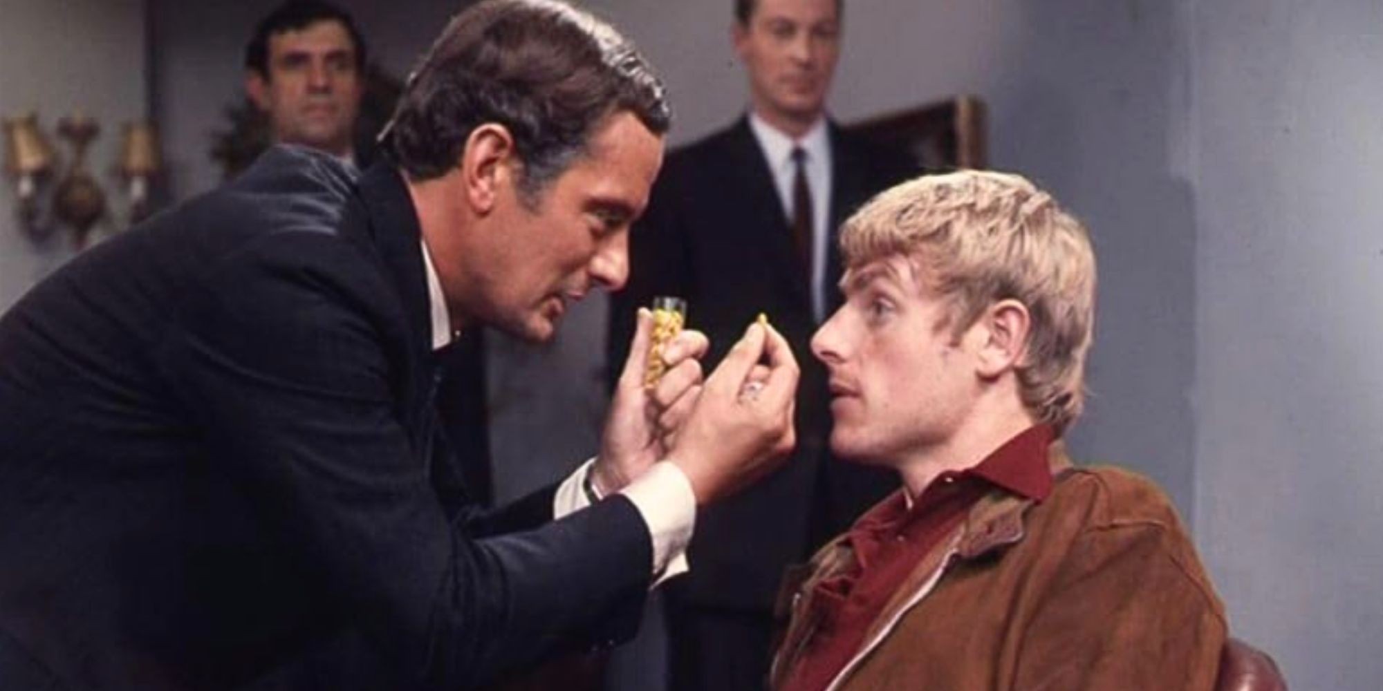 Francis Matthews bends down and holds an object in front of Stephen Bradley in Out of the Unknown.