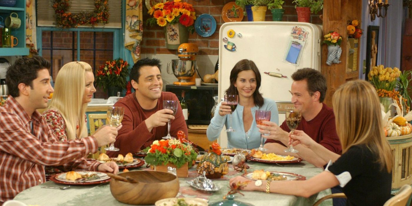 Ross, Phoebe, Joey, Monica, Chandler, and Rachel cheers at the table for Thanksgiving on 'Friends.'