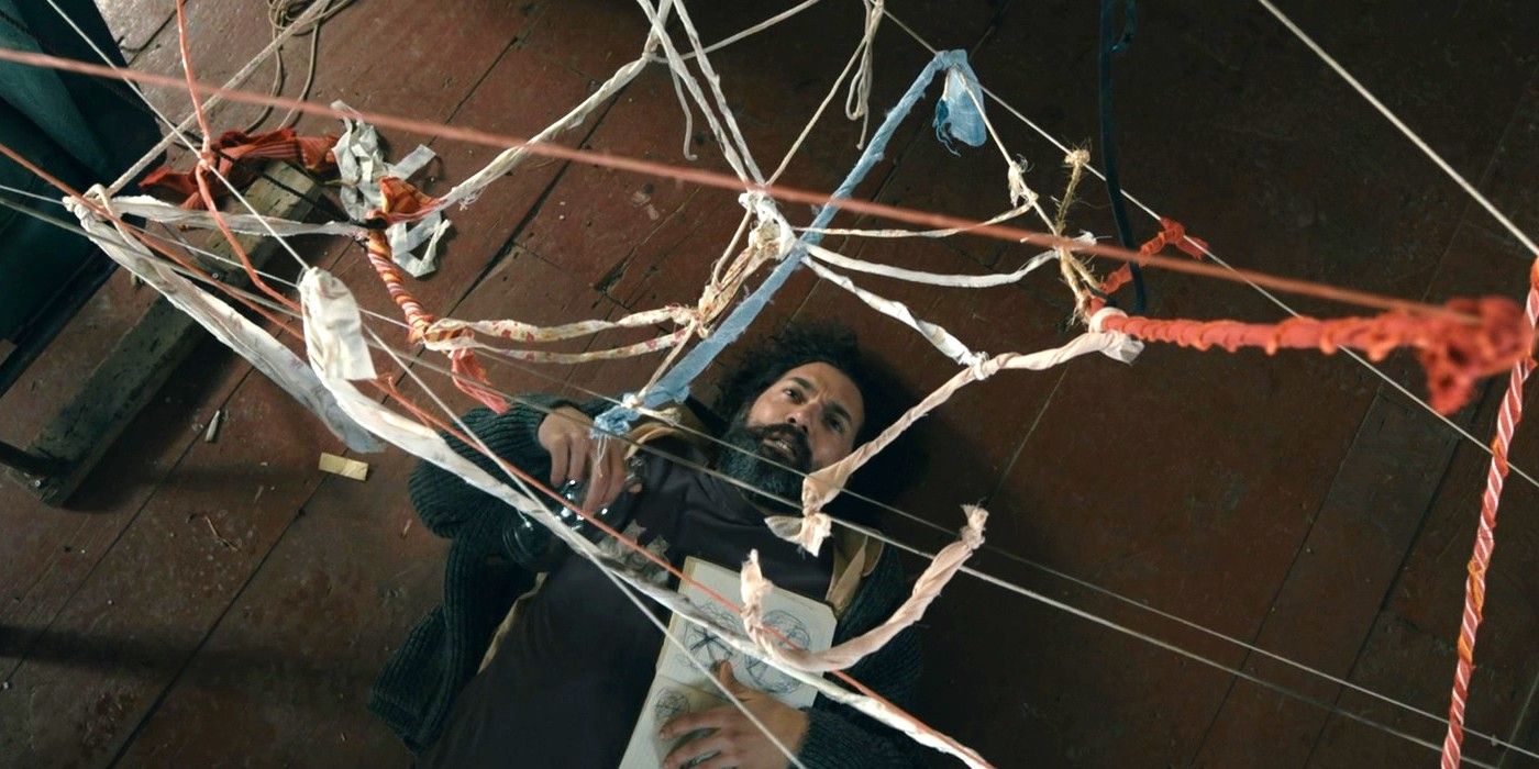 David Alpay as Jade lying on the floor beneath a web of string in 'From' (2022)