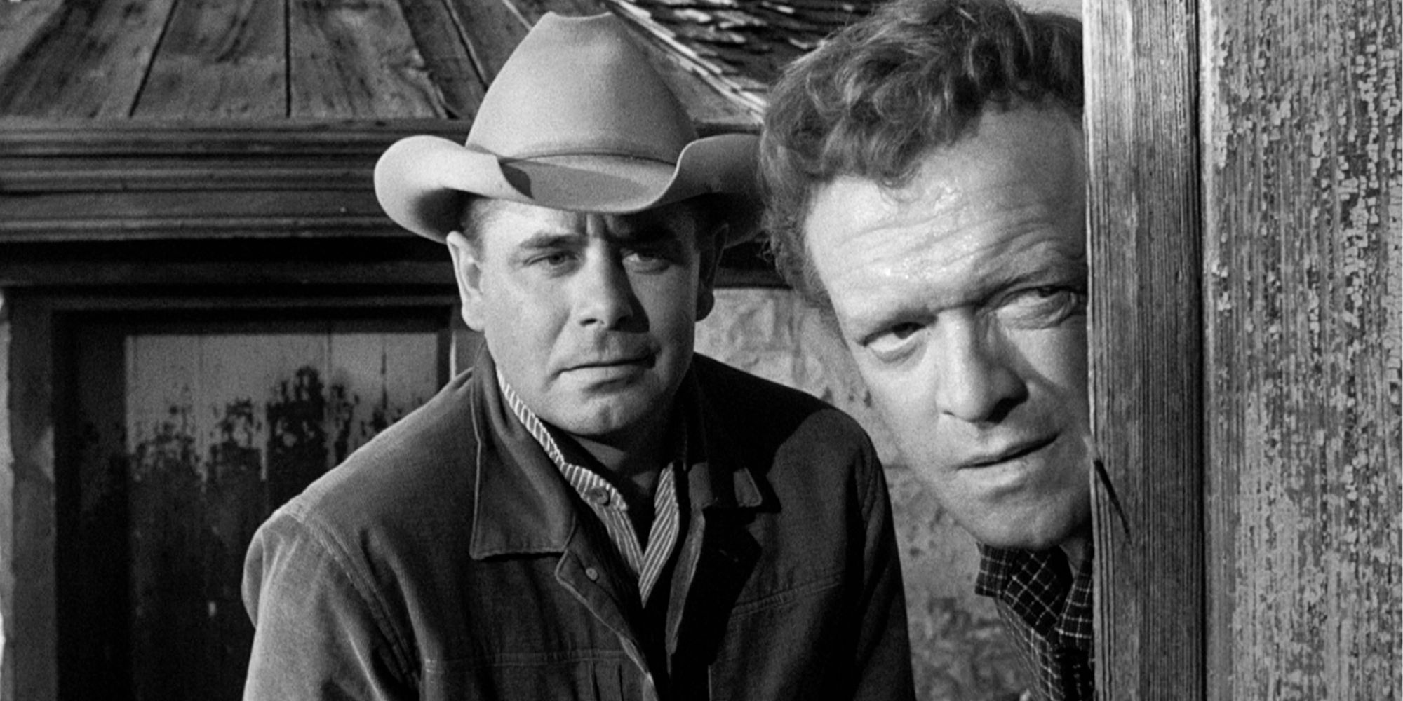 Glenn Ford standing behind Van Heflin who is peering out from behind a structure in 3:10 to Yuma (1957)