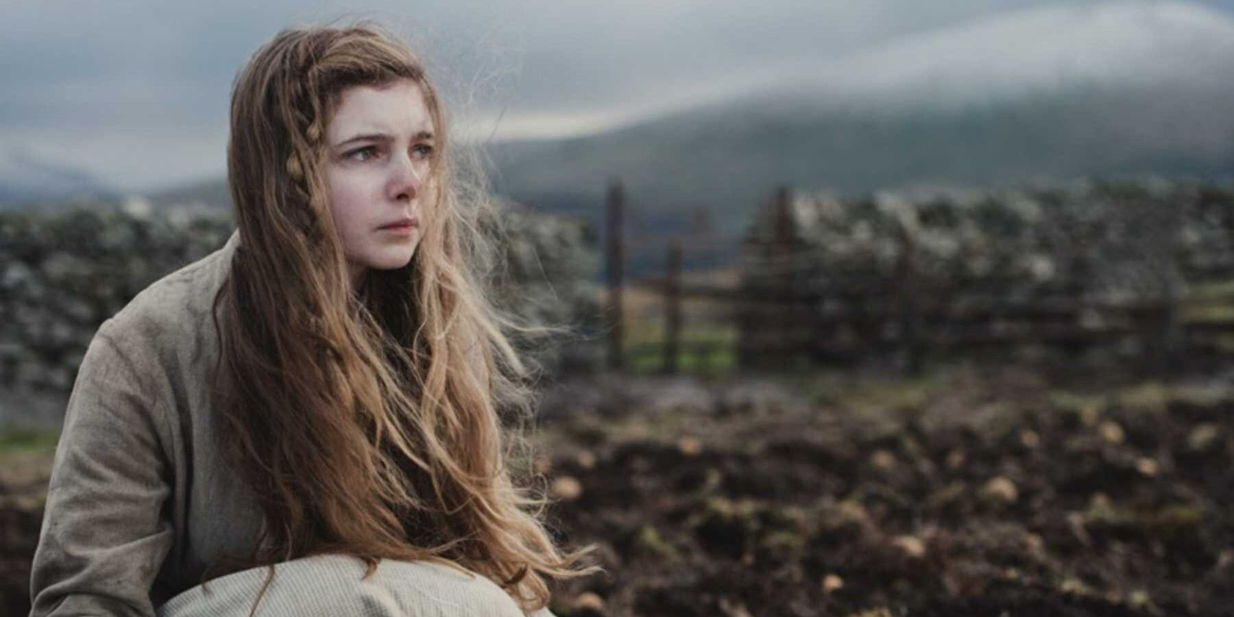 Gwen sits in a field in the movie 'Gwen'