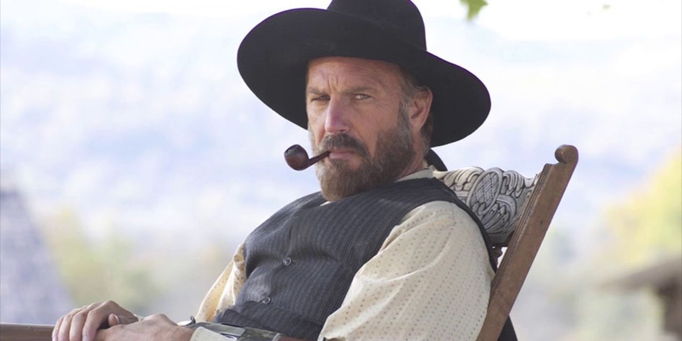 Kevin Costner sitting back in a chair outside with a pipe in his mouth in Hatfields & McCoys.