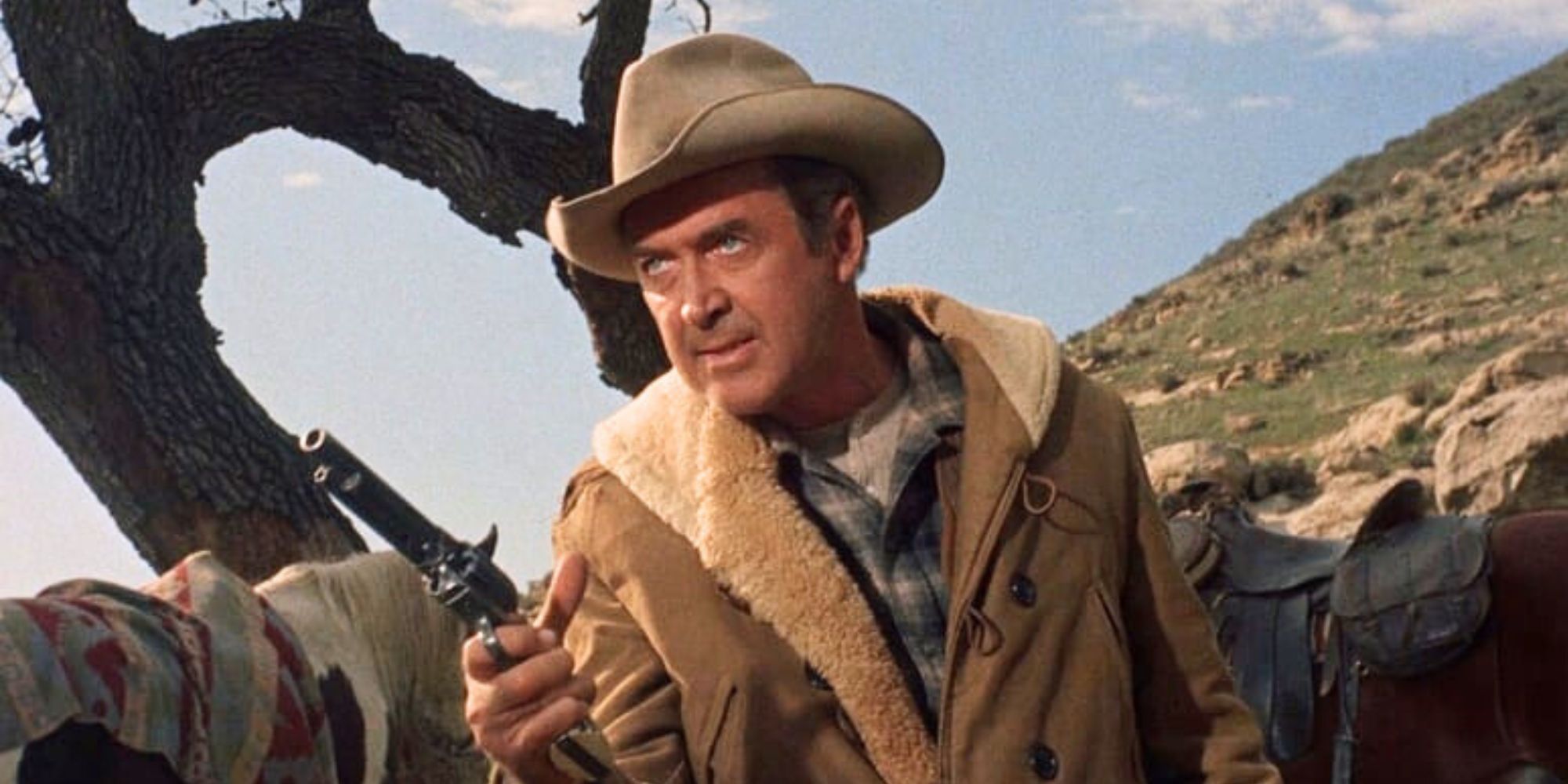 James Stewart wears a cowboy hat and holds a pistol with horses in the background in Two Rode Together (1961)