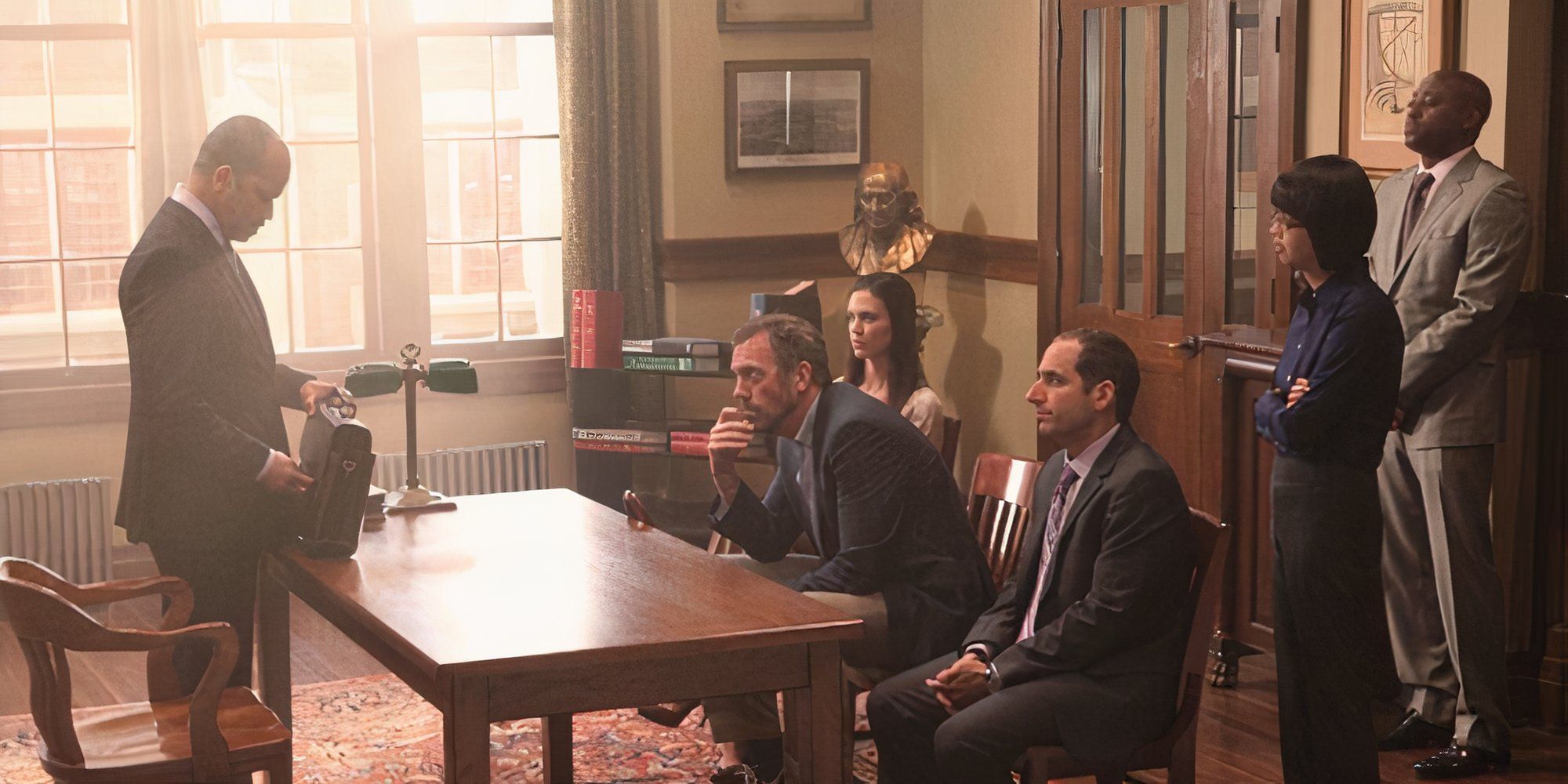 Jeffrey Wright standing on one side of a table while Odette Annable, Hugh Laurie and Peter Jacobson are sitting in chairs on the other side while Omar Epps and Charlyne Yi are standing behind them in House