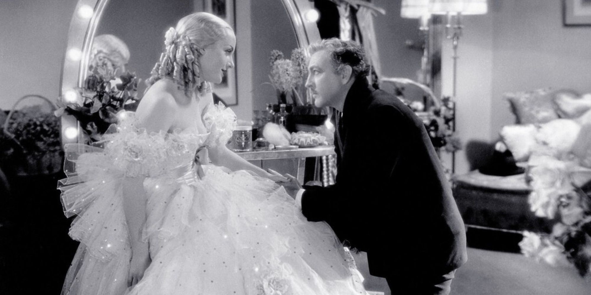 John Barrymore kneeling in front of Carole Lombard who is sitting down in Twentieth Century (1934)