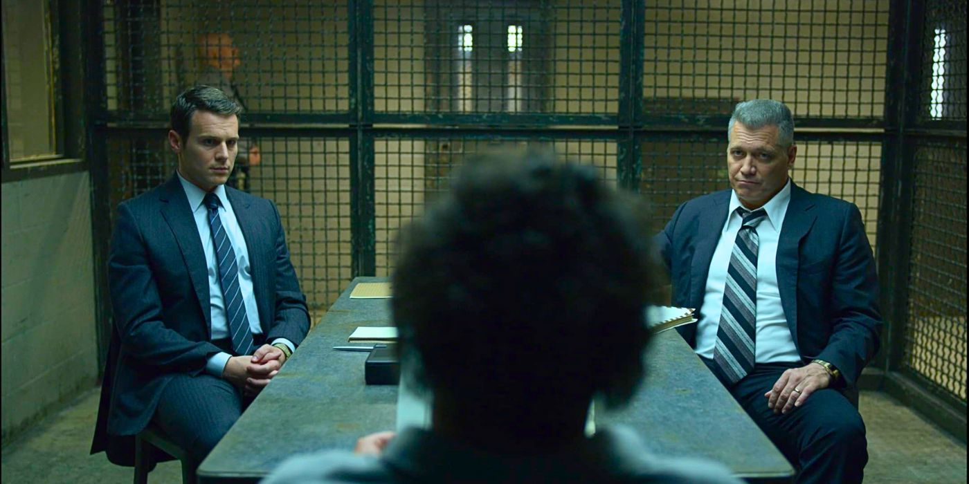 FBI Agent Holden Ford and FBI Agent Bill Tench sit and interview obscured criminal in a prison from the series Mindhunter