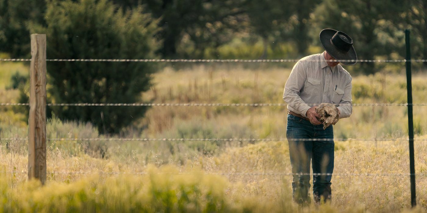 A man wearing a cowboy hat fixes a barbed wire fence