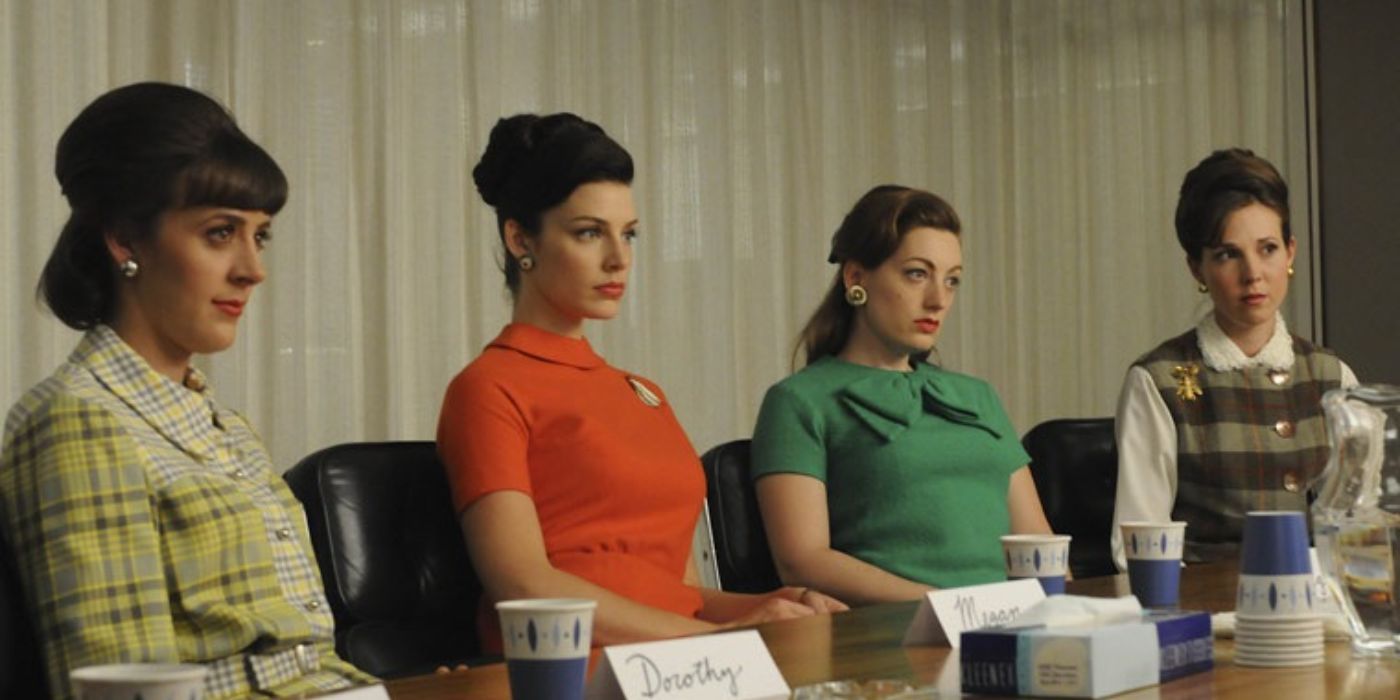 A group of women sit at a long conference table with solemn expressions on their faces in Mad Men.