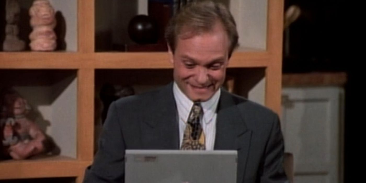 Niles smiles as he starts to type on his computer. He is sitting at a table in Frasier&rsquo;s dining room.