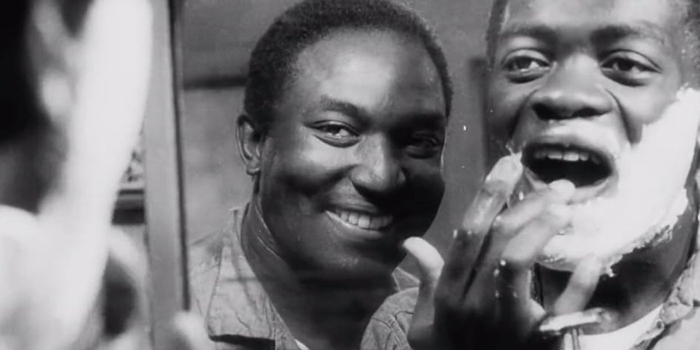A man watches another man shaving his face in the mirror