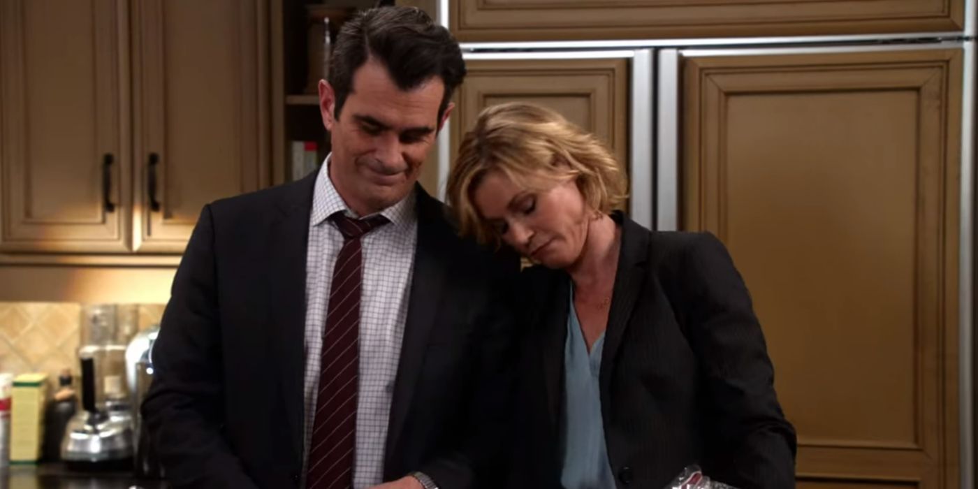 Phil and Claire stand in their kitchen smiling softly as Claire rests her head on Phil&rsquo;s shoulder in Modern Family.