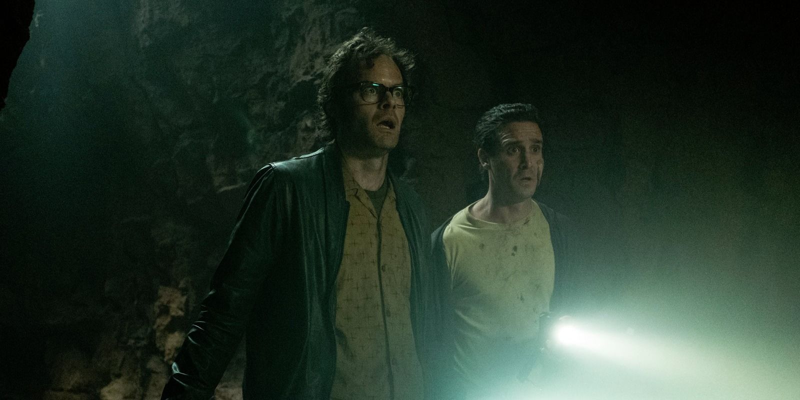 Bill Hader as Richie and James Ransone as Eddie look shocked, holding a flashlight in the dark in It Chapter 2