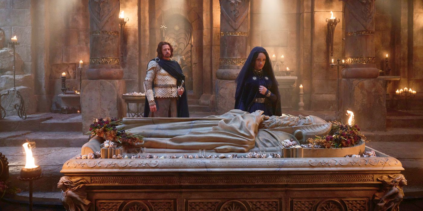 A aide shot of Miriel (Cynthia Addai-Robinson) standing at her father's tomb in a dark mourning outfit with Elendil (Lloyd Owen) standing several steps behind her and to her left in his white armor and cloak in Rings of Power Season 2