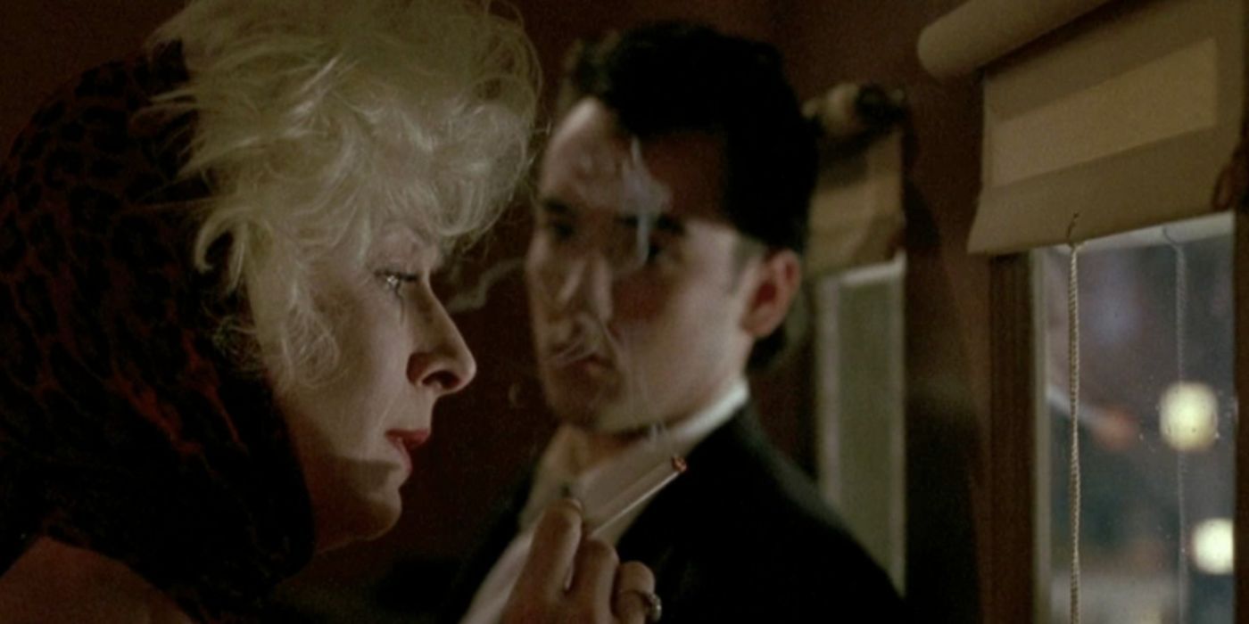 Anjelica Huston and John Cusack as Lilly and Roy Dillon standing in a room smoking a cigarette in 'The Grifters'