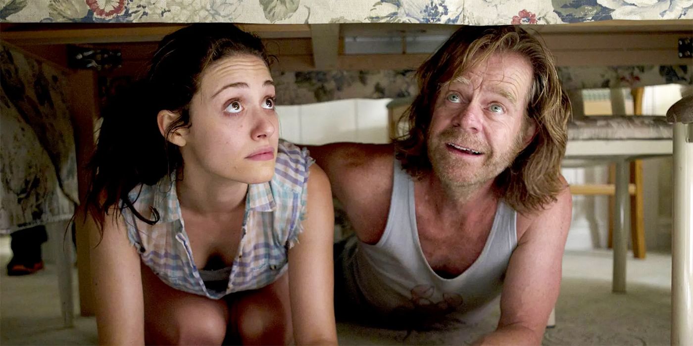 Emmy Rossum as Fiona Gallagher crouched next to William H. Macy as Frank under a table in Shameless
