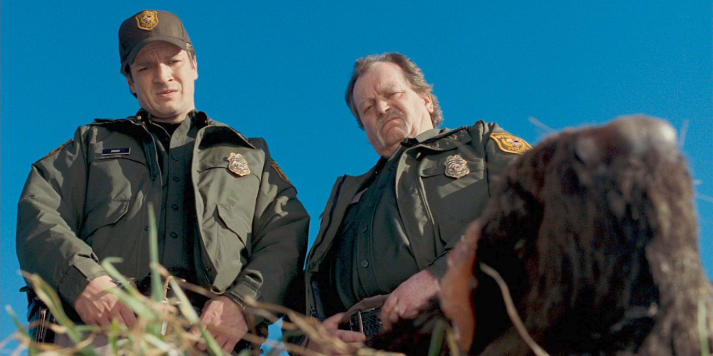 Nathan Fillion as police chief Bill Purdy and another officer stare down at something in Slither.