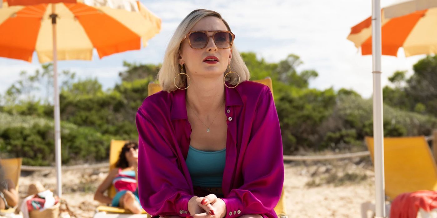 Sophie Turner sitting on a beach chair, wearing sunglasses and a colorful outfit in 'Joan' Series.