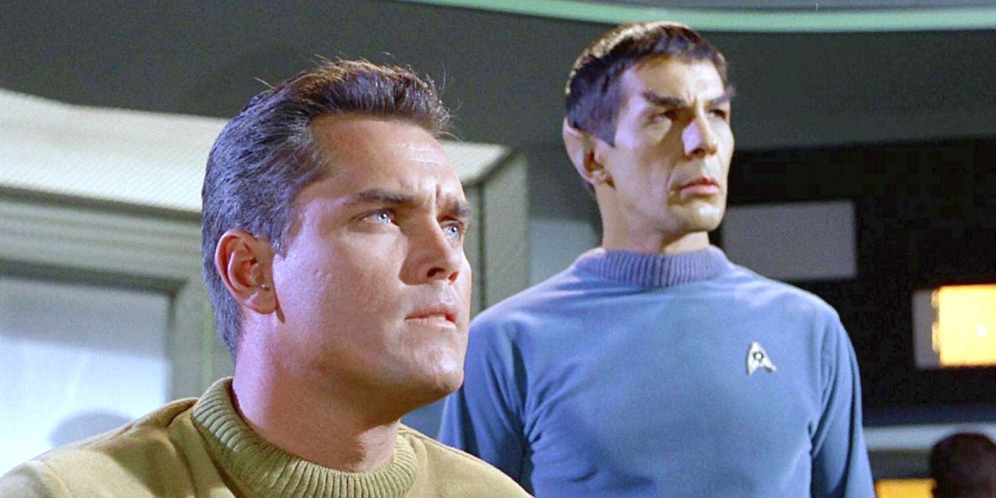 Captain Pike (Jeffrey Hunter) sitting on the bridge with Spock (Leonard Nimoy) standing behind his right shoulder as both men stare ahead at something offscreen to the right in Star Trek: The Original Series