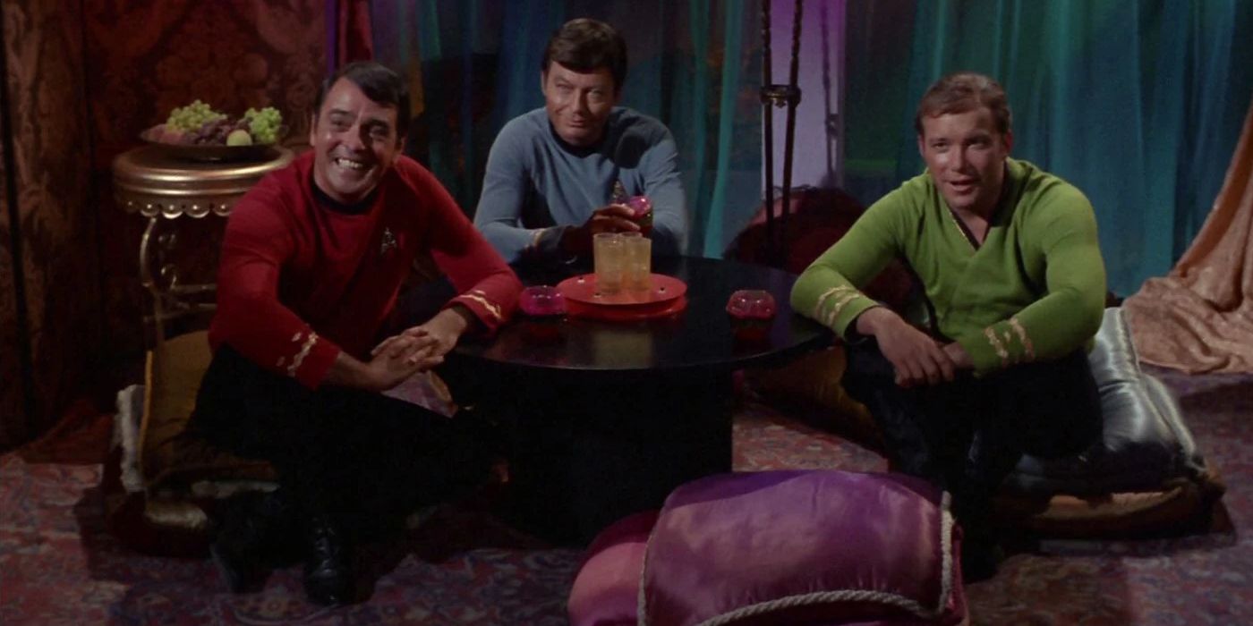 Bones, Kirk, and a third crew member sit on the floor on cushions around a low table in Stark Trek.