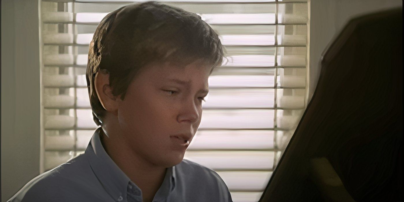 A young River Phoenix as Philip Brogan sitting at a piano and looking sad in Surviving