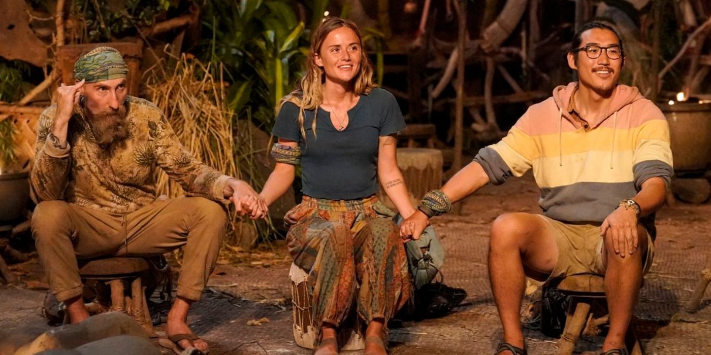 The final three contestants of Survivor 43 hold hands and sit on stumps waiting for the outcome on Survivor.