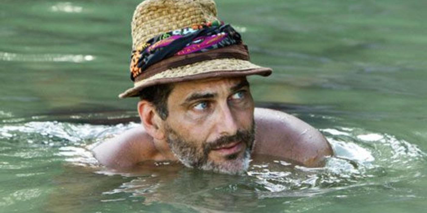 Jonathan Penner swims in water wearing a hat with a bandanna around it in Survivor.