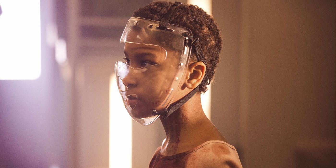 A young black girl with short heart wearing a transparent mask and looking sideways.